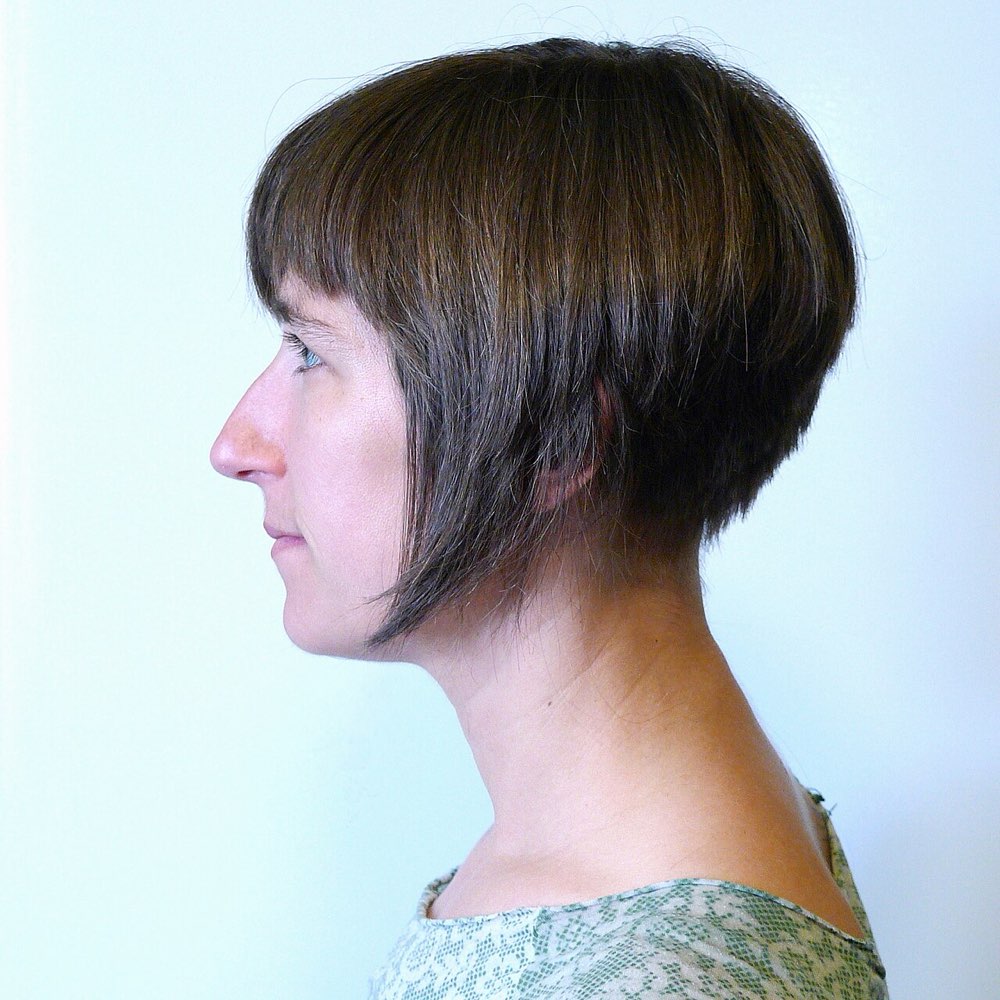 Side view of a woman with a short inverted bob and a side-swept fringe, the front pieces angled down toward the jaw